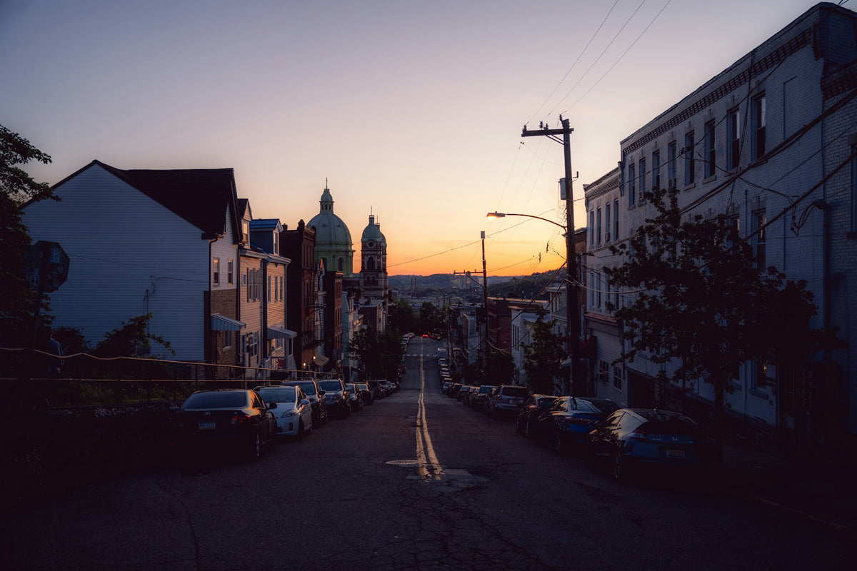 A city street dropping downhill at sunset